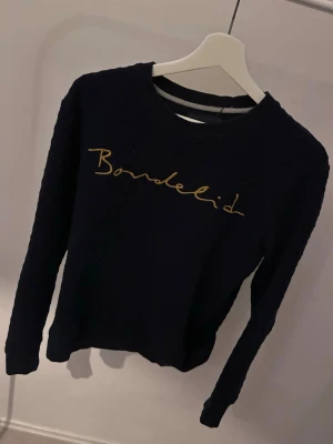 Svart tröja från Bondelid - Snygg svart långärmad tröja från Bondelid med gul soppskrift på bröstet. Klassisk rund halsringning och mjukt material som passar perfekt till jeans eller kjol. Enkel men stilren design som funkar året runt.