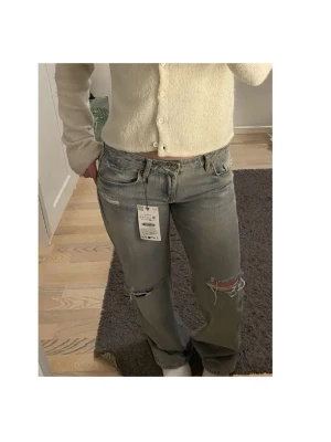 Zara jeans storlek 36 - Snygga grå zara jeans med slitningar och hål på knäna. Klassisk femficksmodell med raka ben och låg midja. Perfekta för en avslappnad och trendig look. Aldrig använda. 
