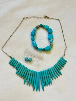 Turkost smyckeset med halsband örhängen och armband  - Snyggt set med turkost halsband med spetsiga hängen, matchande armband med oregelbundna pärlor och glittriga turkosa örhängen. Halsbandet har silverfärgad kedja och armbandet är elastiskt. Perfekt för dig som gillar färgstarka accessoarer.