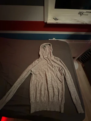  Kashmir tröja  - Grå hoodie i mjukt material med huva och dragsko. Ärmarna har tumhål för extra komfort och en avslappnad look. Perfekt för dig som gillar en enkel och stilren stil. Det finns 2 små hål i luvan. Ny pris 1199! Märke Bvaldi 