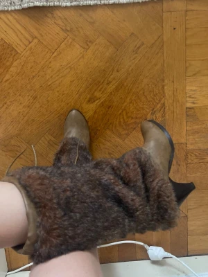 Bruna stövlar med fuskpäls och klack i storlek 40!! - Unika bruna stövlar med hög klack och rund tå. Skaftet är täckt av mjuk fuskpäls som ger en cool och trendig look. Perfekta för dig som vill sticka ut och hålla värmen under höst och vinter. Stängs med snörning upptill.