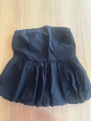 Svart armlös volangtopp - Svart armlös volangtopp. Toppen har en ballongformad siluett och resår upptill för extra komfort. Perfekt för dig som gillar en trendig och enkel stil. Tillverkad i bomull för en skön känsla.