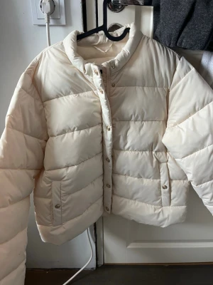 Vit jacka med guld detaljer - Vit nästan dunjacka i storlek Medium med guld detaljer. Inte så tjock så skulle säga att det är med en vår/höst jacka. Aldrig använd så jätte bra skick, märket är okänt