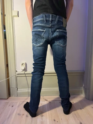 Blå Replay jeans - Säljer ett par blå slim fit jeans från Replay med tydliga vita kontrastsömmar och snygga detaljer på bakfickorna. Jeansen har normal midja och klassisk femficksdesign. Perfekta för dig som gillar en smalare passform och stilrena detaljer.Använd 1 gång för bilderna