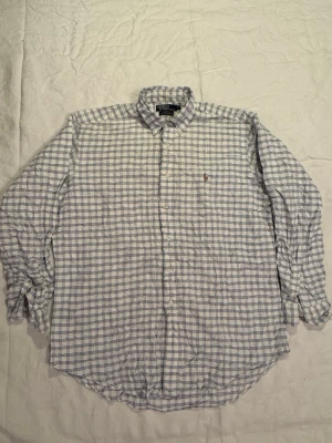 Rutig skjorta från Polo Ralph Lauren - Klassisk rutig skjorta från Polo Ralph Lauren i vitt och blått. Skjortan har lång ärm, knappar framtill och button-down krage. Tillverkad i 100% bomull och har den ikoniska broderade loggan på bröstet. Perfekt för en stilren och avslappnad look.