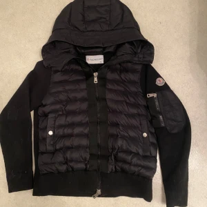 Svart pufferjacka med huva från Moncler - Säljer en riktigt snygg moncler cardigan som ser sprillans ny ut. Mycket skön inför kalla dagar på sommaren till exemel moln osv.