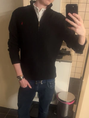 Ralph lauren kabelstickad - Säljer en svart stickad tröja från Polo Ralph Lauren med halv dragkedja och hög krage. Tröjan har ett diskret kabelstickat mönster och den klassiska röda loggan broderad på bröstet. Perfekt till jeans eller chinos för en clean look.