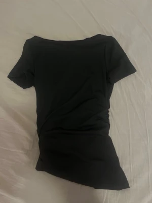 Svart topp med spets och rosett - Svart kortärmad topp med snygg spetsdetalj och rosett i ryggen från shein. Toppen har en öppen rygg med blommönstrad spets och en feminin knytdetalj. Perfekt för dig som gillar unika detaljer och stilren look.