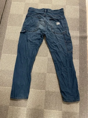 Blå jeans från Lee med raka ben - Snygga blå jeans från Lee med raka ben och klassiska fickor både fram och bak. Jeansen har en extra sidoficka och är tillverkade i mjukt denimtyg. Perfekta för en avslappnad och trendig look. Passformen är straight och storlek W31 L32