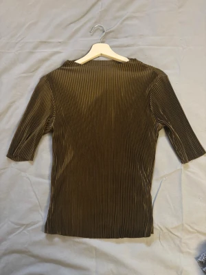 Grön ribbad topp med trekvartsärm - Snygg mörkgrön topp med ribbad struktur och trekvartsärm. Materialet känns mjukt och stretchigt, perfekt för en stilren look. Passformen är normal och toppen har en enkel, klassisk design utan synliga detaljer framtill.