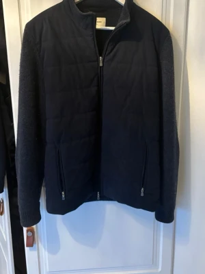 Mörkblå cardigan jacka Gran Sasso - Stilren mörkblå cardigan jacka från Gran Sasso. Jackan har quiltad front, stickade ärmar och två dragkedjeförsedda fickor. Perfekt för lager på lager och ger en clean look till din outfit.