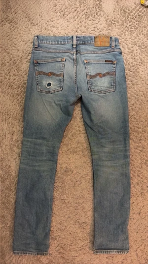 Ljusblå jeans från Nudie Jeans - Snygga ljusblå jeans från Nudie Jeans.  Har ett  hål på bakfickan. Jeansen har en slim passform, modell Lean Dean. Storlek 31/30 Längd 99cm, midja 43cm,