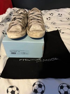 Philippe Model vita sneakers, strl 39 - Snygga vita sneakers från Philippe Model med klassisk låg profil och snörning. Skorna har en slitstark ovandel i skinn och detaljer i beige. Perfekta för dig som gillar en stilren och trendig look.