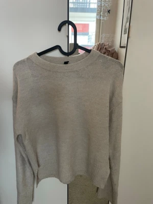 Beige stickad tröja från H&M - En enkel och stilren beige stickad tröja från H&M. Tröjan har rund halsringning, långa ärmar och ribbade muddar vid ärmslut och nederkant. Perfekt att matcha med jeans eller kjol för en avslappnad look.