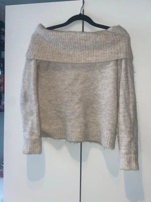 Beige off shoulder stickad tröja Gina Tricot - Säljer en beige stickad off shoulder-tröja från Gina Tricot. Tröjan har bred ribbad kant upptill som kan bäras nedanför axlarna, samt ribbade muddar vid ärmslut och nederkant. Mjuk och fluffig känsla, perfekt för en trendig look.