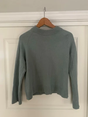 Ljusgrön stickad tröja från Wera - Mysig ljusgrön stickad tröja från Wera med hög ribbad hals och långa ärmar. Tröjan har en avslappnad passform och ribbade muddar vid ärmslut och nederkant. Perfekt för lager på lager och enkel att styla till olika looks.
