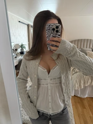 Ljusgrå kabelstickad Brandy Melville kofta - Ljusgrå kabelstickad kofta med rund halsringning och vita knappar framtill. Koftan har långa ärmar och ribbade muddar vid ärmslut och nederkant. Perfekt att slänga över en topp för en snygg lager-på-lager-look💕är one Size men passar som en small