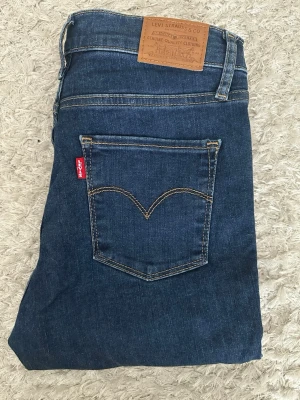 Levi's 720 High Rise Super Skinny Jeans W27L30 - Snygga blå Levi's 720 High Rise Super Skinny jeans med klassisk femficksdesign och hög midja. Jeansen har en smal passform och är tillverkade i stretchig denim för extra komfort. Perfekta för dig som gillar en tight och modern look.