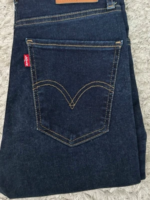 Levi's mörkblå jeans mile high super skinny W27L30 - Mörkblå jeans från Levi's med den ikoniska röda loggan på bakfickan och snygga kontrastsömmar. Klassisk rak modell i jeansmaterial, perfekt för en stilren look. Passar dig som gillar tidlös denim.