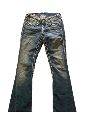 Blå bootcut jeans med kontrastsömmar - Snygga blå jeans med tydliga vita kontrastsömmar och bootcut (lågmidjade). Midjemått rakt över: 32   Innerbenslängd: 73     Pris går att diskutera.