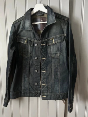 Mörkblå jeansjacka från G-Star RAW - Snygg mörkblå jeansjacka från G-Star RAW, modell 3301. Klassisk design med kontrastsömmar, bröstfickor med knappar och detaljer i metall. Jackan har en rak passform och är perfekt för dig som gillar streetwear och denim.