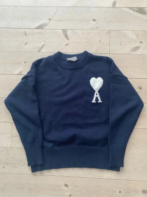 Mörkblå stickad tröja från Ami - Mörkblå stickad tröja från Ami Alexandre Mattiussi med rund halsringning och ribbade muddar. Tröjan är i storlek M men skulle säga att den är lite liten i storleken. Skicket är fantastiskt, den är i princip helt oanvänd.