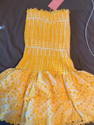 Gul kortklänning med volang - Söt gul kortklänning med smockad överdel och volangig kjol. Klänningen har ett lekfullt mönster och är axelbandslös, perfekt för varma dagar. Tillverkad i ett lätt material som känns skönt mot huden.Köpte till skolavslutningen men gillade inte hur den satt på mig men hann inte lämna tillbaks. Så helt oanvänd alltså endast testad på. Lappen är kvar och man får den i original påsen därav går det inte att förhandla ner så nycker! 