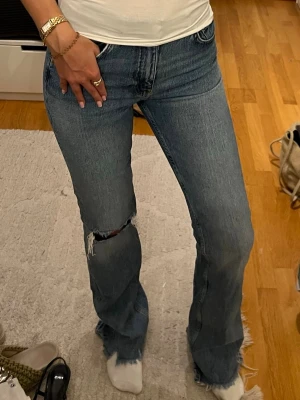 Blå bootcut jeans  - Säljer ett par blå jeans med bootcut passform och ett hål vid knät samt fransiga benslut. Mina absoluta favorit jeans som inte säljs längre, dessa är mer en 34 än en 32. Brukar ha 34-36 i jeans o dessa passar mig!💞❤️🥰 