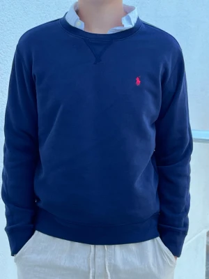 Mörkblå Polo Ralph Lauren tröja - Riktigt schysst mörkblå tröja från Polo Ralph Lauren med rund halsringning och röd logga utan luva. 