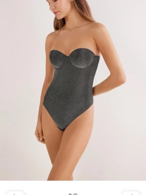 Glittrig svart body med bygel - Snygg svart body med glittrigt tyg och bygelkupor för extra stöd. Axelbandslös modell med knäppning i grenen. Perfekt att styla till jeans eller kjol för en cool look. Aldrig använd. Från intimissimi. Ursprungspris 700kr 