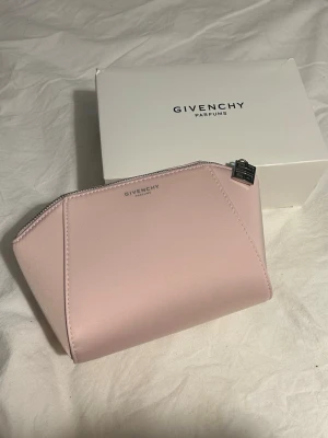 Rosa necessär från Givenchy - Supersöt necessär från Givenchy i ljusrosa satinliknande material. Väskan har en stilren form med silverfärgad dragkedja och Givenchy-logga i metall framtill. Perfekt storlek för smink eller småprylar och känns riktigt lyxig.