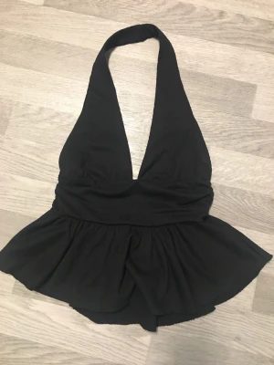 Svart urringad topp med volang - Säljer en svart topp från ZARA med djup v-ringning och bar rygg. Toppen  har en markerad midja och volang nedtill för en snygg siluett. Perfekt att styla till jeans eller kjol för en trendig look.Strl M.