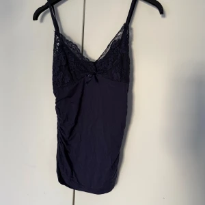 Mörkblå spetsdetaljerad linnetopp - Säljer en mörkblå linnetopp med tunna axelband och v-ringad spets upptill. Materialet känns mjukt och toppen har rynkade sidor för extra snygg passform. Aldrig använd 