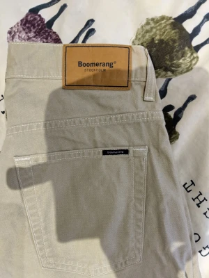 Beige jeans från Boomerang - Säljer ett par klassiska beige jeans från Boomerang. Byxorna har raka ben, normal passform och fem fickor. Tillverkade i mjuk bomull med bälteshällor och diskret Boomerang-logga ovanför bakfickan. Perfekta till en avslappnad stil.