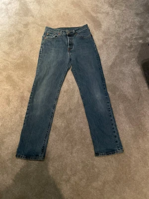 Levi's 501 blå jeans straight fit - Klassiska blå Levi's 501 jeans med rak passform och femficksdesign. Jeansen har normal midja och är tillverkade i slitstarkt bomullsjeans. Perfekta för dig som gillar en tidlös och avslappnad look.