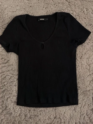 Svart ribbad tröja från Bikbok - Säljer en svart ribbad tröja i storlek S. Det är en basic tröja som passar till allt. En liten detalj i fram på bröstet som gör att plagget ser lite mer uppklätt ut.