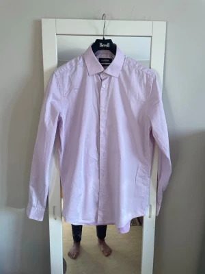 Ljuslila skjorta från Dressmann M - Säljer en stilren ljuslila skjorta från Dressmann i storlek M. Skjortan är tillverkad i 100% bomull, har klassisk krage, långa ärmar och knäppning framtill. Perfekt för dig som gillar en clean och enkel look.den är sliim fit