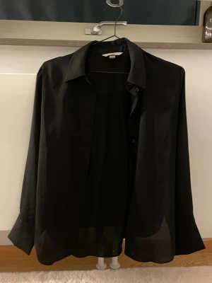 Svart blus från H&M - Elegant svart blus från H&M i storlek XS, passar även S. Lätt att matcha med både vardagskläder och festliga outfits. Använd endast två gånger och i fint skick. Ett stilrent basplagg som alltid fungerar.