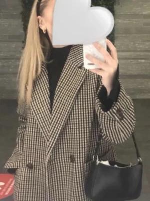 Rutig oversized kappa i brunt och beige - Säljer en oversized kappa med rutigt mönster i brunt och beige. Jackan har bred krage, dubbelknäppning med stora knappar och långa ärmar. Perfekt för dig som gillar en trendig och avslappnad look.