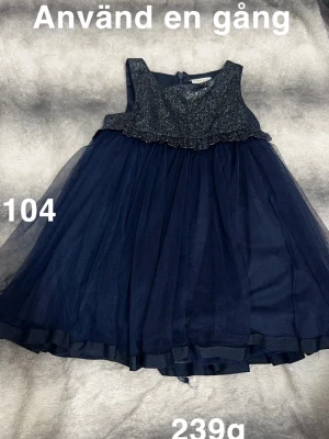 Mörkblå glittrig barnklänning - Supersöt mörkblå klänning med glittrigt liv och volangdetalj. Kjolen är fluffig i flera lager tyll och klänningen är ärmlös. Perfekt för speciella tillfällen när man vill känna sig extra fin.🌸 Använd en gång. Storlek 104
