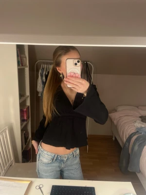 Svart v-ringad blus/topp med knytband - Säljer en svart blus/topp  med v-ringning och långa ärmar. Toppen har ett knytband i midjan som knyts baktill och ger en snygg siluett. Materialet känns mjukt och lätt, perfekt att styla med jeans eller kjol.