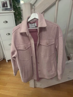 Ljusrosa overshirt från Stradivarius - Säljer en ljusrosa overshirt från Stradivarius i storlek S. Jackan har två stora bröstfickor med knappar, klassisk krage och knäppning framtill. Materialet känns mjukt och har en ull-liknande finish. Perfekt att slänga över en hoodie eller t-shirt.