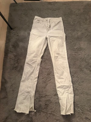Vita raka jeans från Zara med slits - Säljer ett par vita jeans från Zara i rak modell med hög midja. Byxorna har råa, fransiga benslut och slitsar längst ner för en edgy vibe. Klassisk femficksdesign och tillverkade i bomull. Perfekta till sneakers eller boots. Själv så är jag 176 med långa ben och är lite för korta för mig