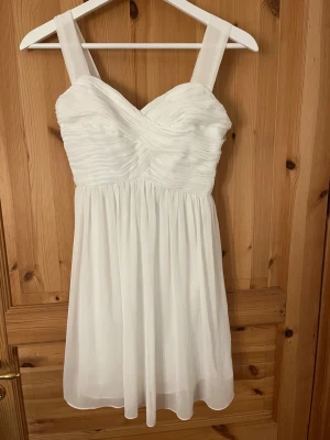 Vit kortklänning från NLY One - Supersöt vit kortklänning från NLY One i storlek 34. Klänningen har breda axelband, draperad överdel och lätt utställd kjol. Tillverkad i ett tunt, flowy material med dragkedja i sidan för enkel påklädning. Perfekt för sommarens alla tillfällen! Inga defekter och pris är förhandlingsbart! Skriv om ni har frågor eller vill veta mått!! Postar inom 1-2 dagar💕