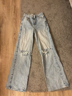 Jeans i storlek XXS från Gina Tricot - Säljer ett par ljusblå Jeans från Gina Tricot i storlek XXS. Två hål vid knäna och hyfsat hög midja. Det finns en liten fläck på jeansen kolla bilden.