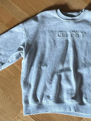 Grå sweatshirt från Aim'n - Säljer en ljusgrå sweatshirt från Aim'n med broderad logga framtill. Tröjan har rund halsringning, ribbade muddar och är tillverkad i en mjuk bomulls- och polyestermix. Perfekt för chill dagar eller till träningen. Syns att den har används.