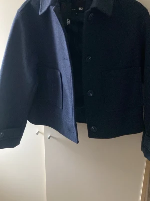Mörkblå kappa från 157, XS - Aldrig använd bar testad!! Prislappen e kvar. Snygg mörkblå kappa från 157 i ullblandning. Klassisk rak modell med krage, stora framfickor och knäppning med knappar. Perfekt för dig som gillar stilrena och tidlösa plagg. Nypris 400 