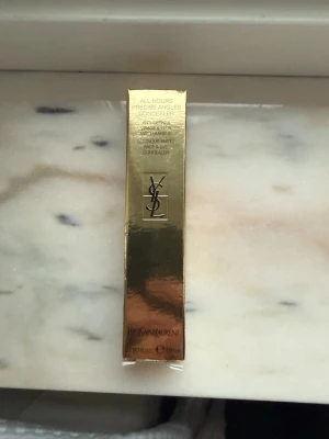 YSL All Hours Precise Angles Concealer - YSL All Hours Precise Angles Concealer i färgen MN1. Kommer i en lyxig guldig förpackning och har en stilren glasflaska med svart lock och guldfärgad YSL-logga. Innehåller 15 ml och ger en matt finish för både ansikte och under ögon. Helt ny och inte använd pga fel färg. 