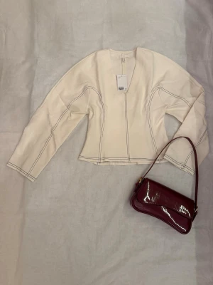 Vit croppad topp med kontrastsömmar - Såldes för 349kr. En vit croppad topp från H&M med markerade svarta kontrastsömmar. Toppen har lång ärm, v-ringad hals och en lätt figurnära passform. Materialet är kraftigare bomull med struktur och toppen har en modern, stilren look.