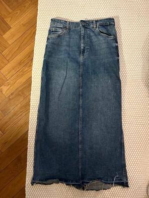 Lång jeanskjol från Zara med slits - Aldrig använt! Säljer en lång jeanskjol från Zara i klassisk blå denim. Kjolen har rå kant nertill, femficksmodell och en snygg slits bak för extra rörelsefrihet. Perfekt till sneakers eller boots för en chill look.